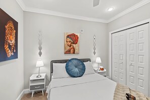 Quarto com cama, duas mesas de cabeceira, um guarda-roupa e obras de arte nas paredes.