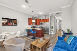 A modern living room with a wooden coffee table, a blue sofa, and a kitchen area with wooden cabinets and stainless steel appliances. - Sleek City Nest 1BD | Walk to N Liberties | Fits 2 (Philadelphia)