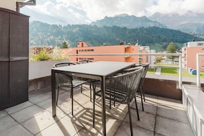 An outdoor terrace with a table and chairs, overlooking a mountainous landscape. - New Listing (Engelberg)