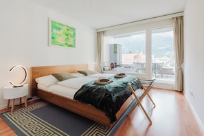 A modern bedroom with a wooden bed, a green abstract painting, and a balcony with a view. - New Listing (Engelberg)