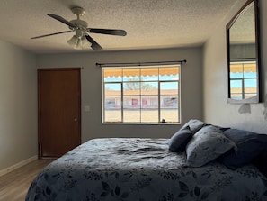 A bedroom with a bed, a ceiling fan, a window with a view, and a door. - A-Town Motel (Arnett)