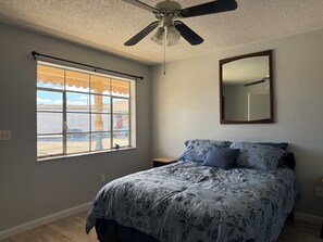 A bedroom with a bed, a ceiling fan, a window with a view, and a mirror on the wall. - A-Town Motel (Arnett)