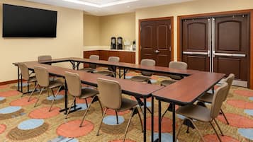 Une salle de conférence équipée d’une longue table, de chaises, d’un téléviseur à écran plat, d’un coin café et de portes à deux battants.