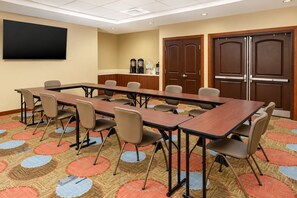 Une salle de conférence équipée d’une longue table, de chaises, d’un téléviseur à écran plat, d’un coin café et de portes à deux battants.