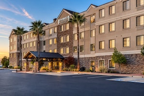 Un hotel de varios pisos con fachada de piedra, entrada cubierta y un cartel que indica 'Staybridge Suites'.