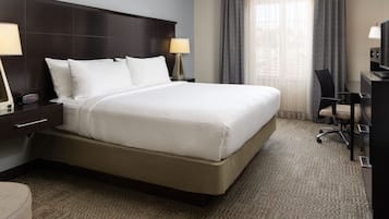 A hotel room with a large bed, two bedside tables with lamps, a desk with a chair, and a television.