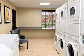 Une buanderie équipée d’une machine à laver et d’un sèche-linge superposés, d’un banc et d’une fenêtre donnant sur les arbres.