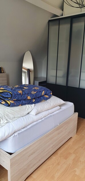 Ein Bett mit einer blauen, gemusterten Decke, einem weißen Kopfkissen und einem Holzkopfbrett.