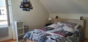 Ein Schlafzimmer mit einem Bett, einem Nachttisch, einer Lampe, einem Wandbild und einem Fenster.
