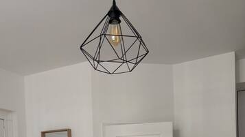 Quarto com porta branca, piso de madeira e luminária pendente geométrica.