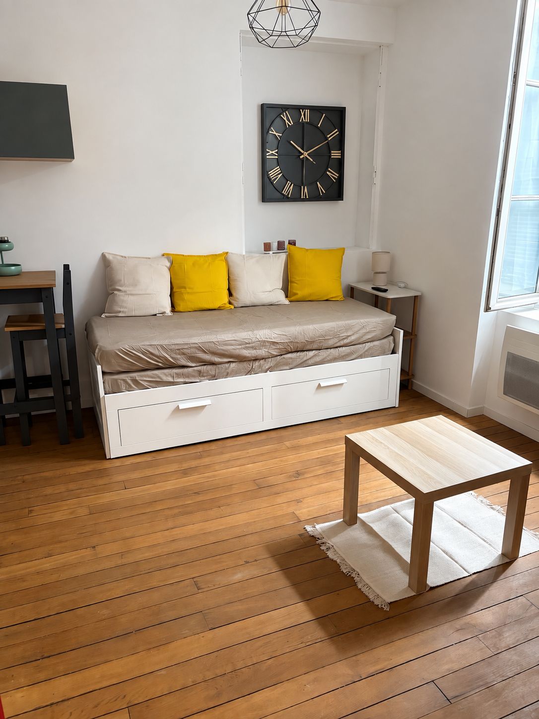 A bedroom with a bed, bedside table, lamp, and a wall clock.