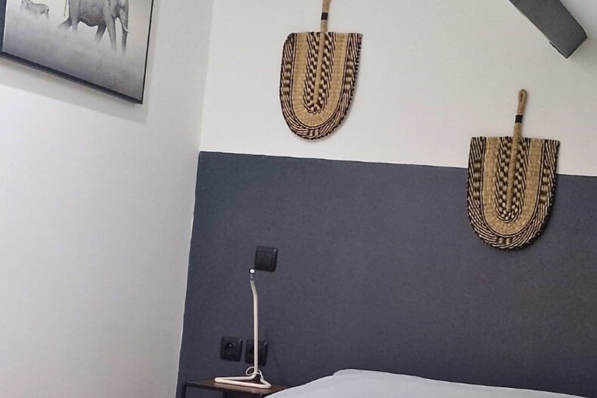 A hotel room with a bed, two wall-mounted decorative items, a nightstand, and a lamp.