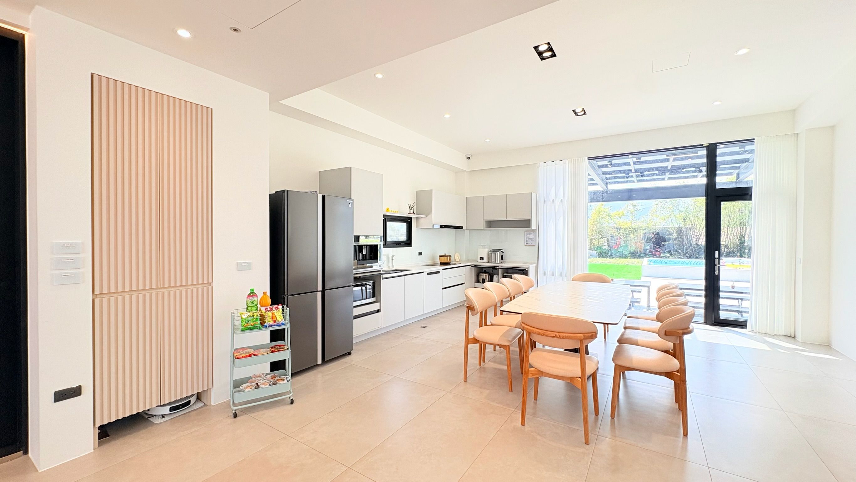 A modern kitchen with a dining area, large windows, and a view of the outdoors.
