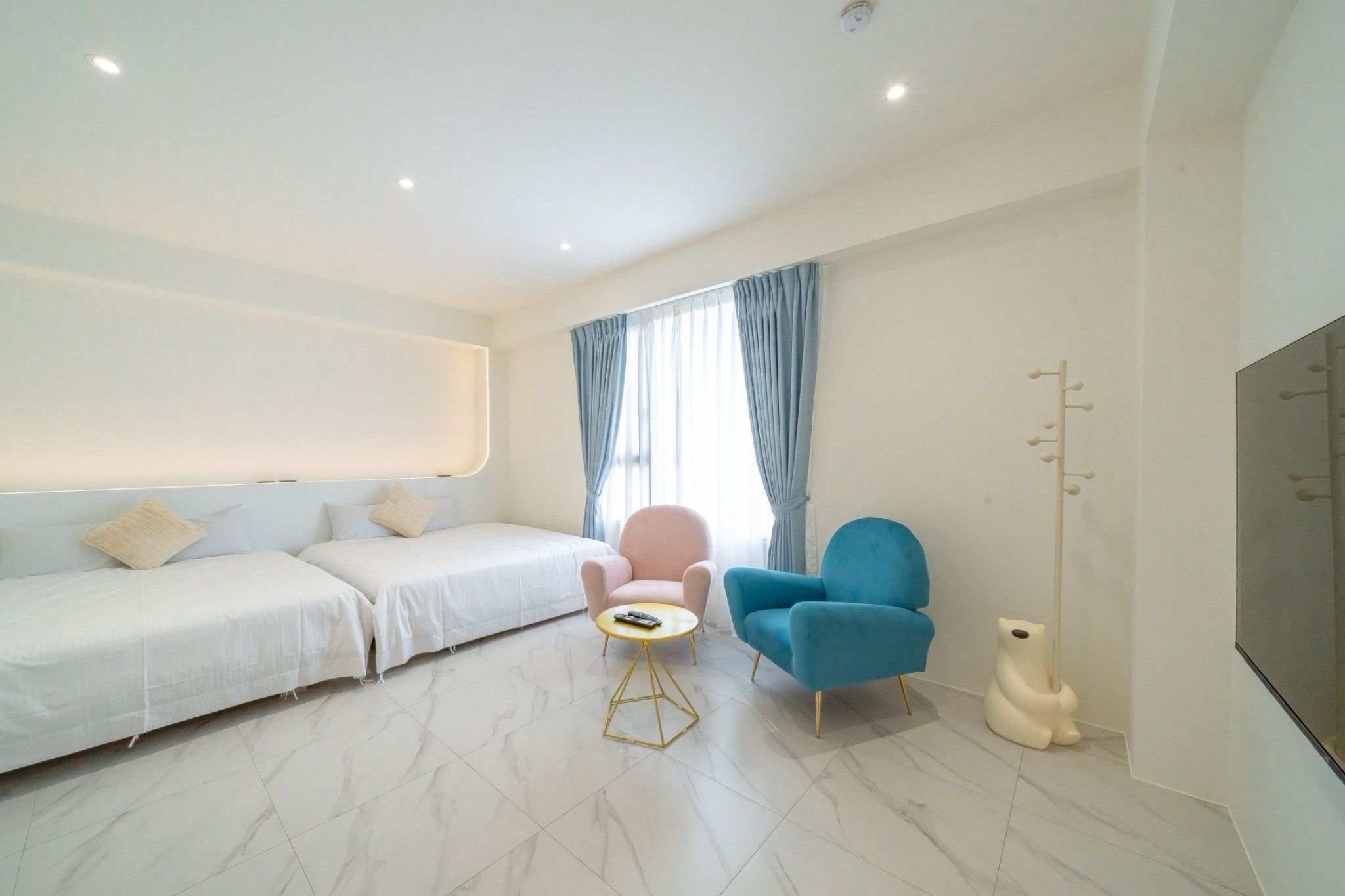Una habitación de hotel moderna con un sofá, dos sillones, una mesita y un televisor.
