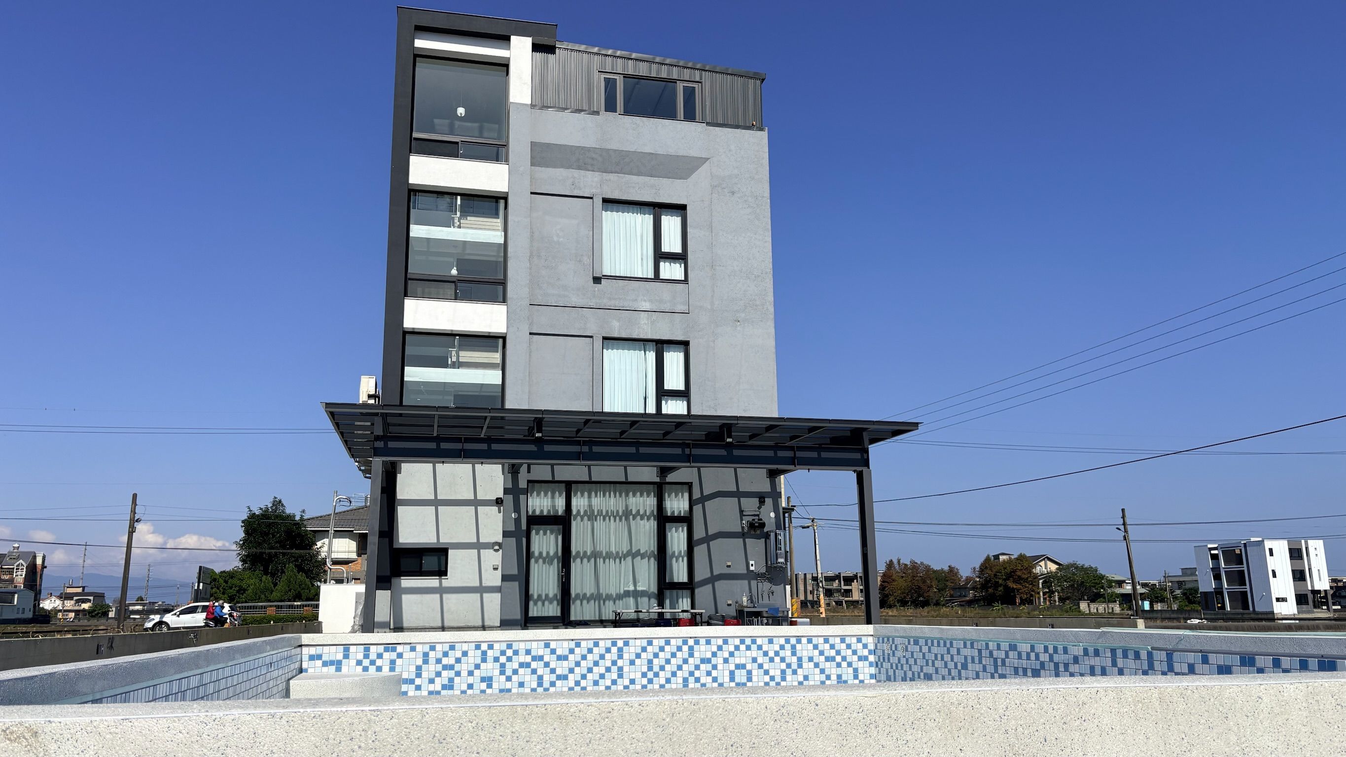 A modern multi-story building with a covered outdoor area and a pool.