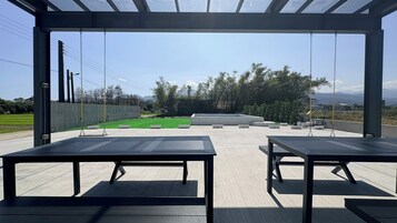 An outdoor seating area with tables and chairs, a view of a landscaped garden, and a clear sky.
