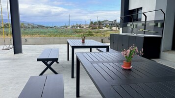 An outdoor patio with two tables and a bench, a small potted plant, and a grill area.