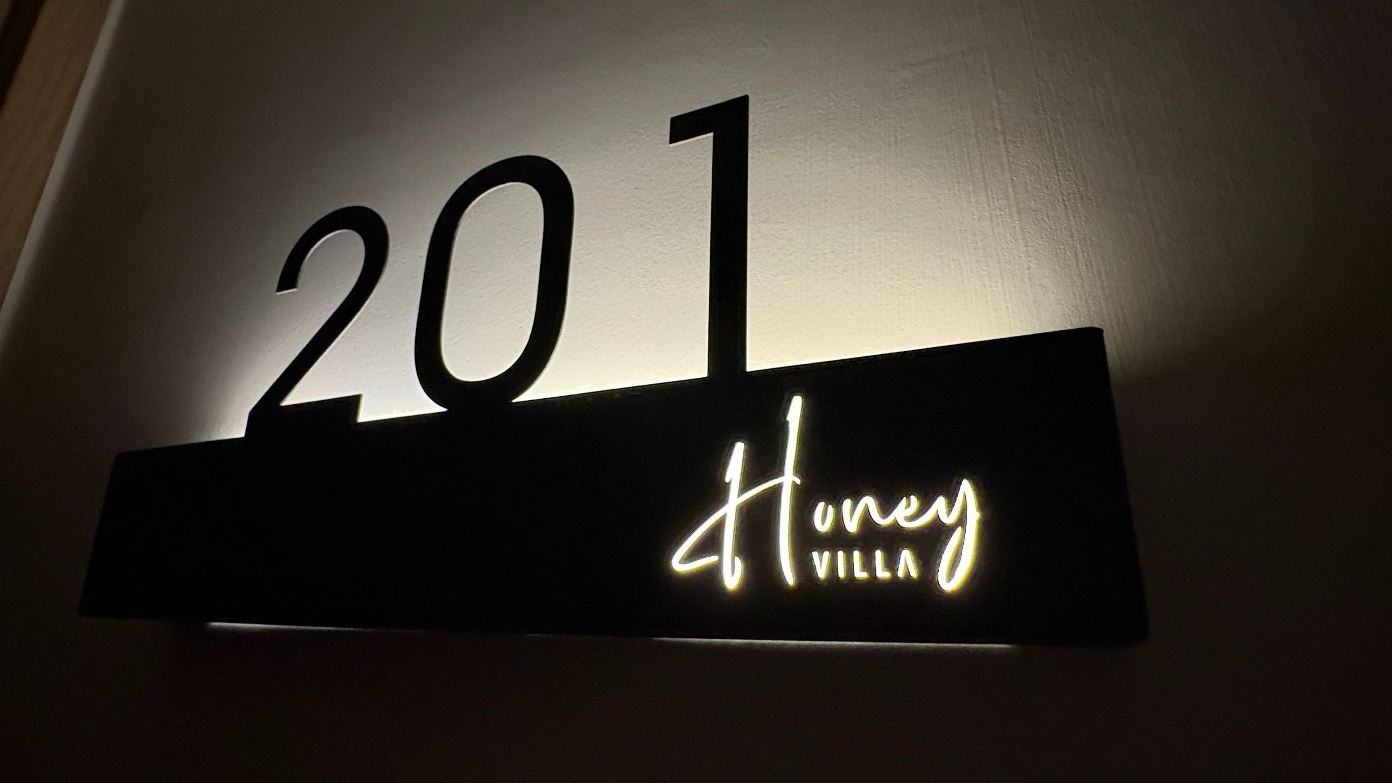 A sign with the number '201' and the name 'Honey Villa' illuminated in white.