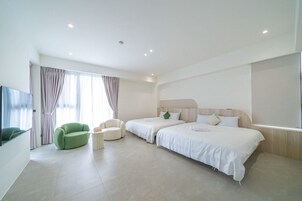 A modern hotel room with a large bed, two bedside tables, a green armchair, and a flat-screen TV.