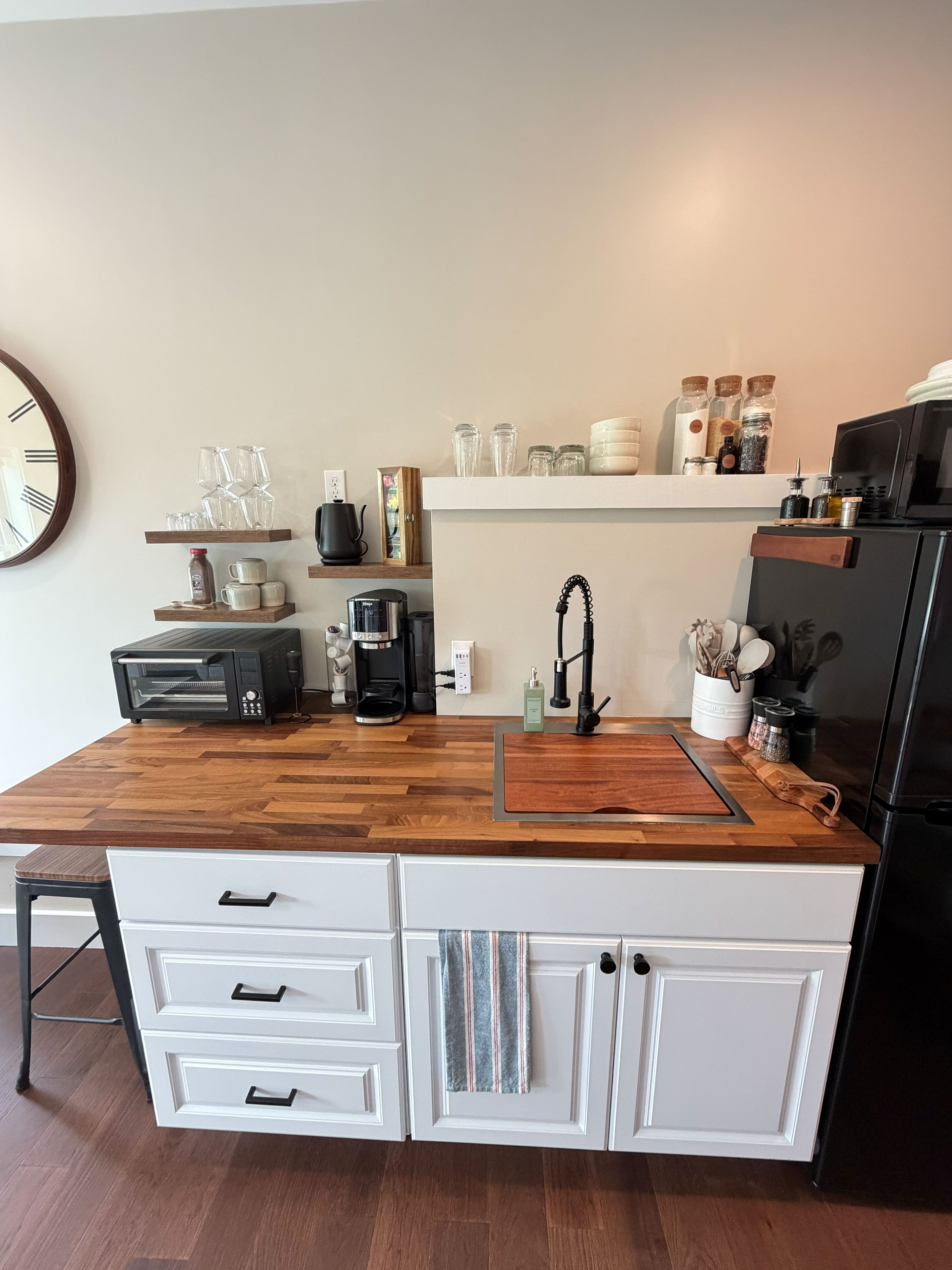 A modern kitchen with a wooden countertop, white cabinetry, a coffee maker, and a microwave.