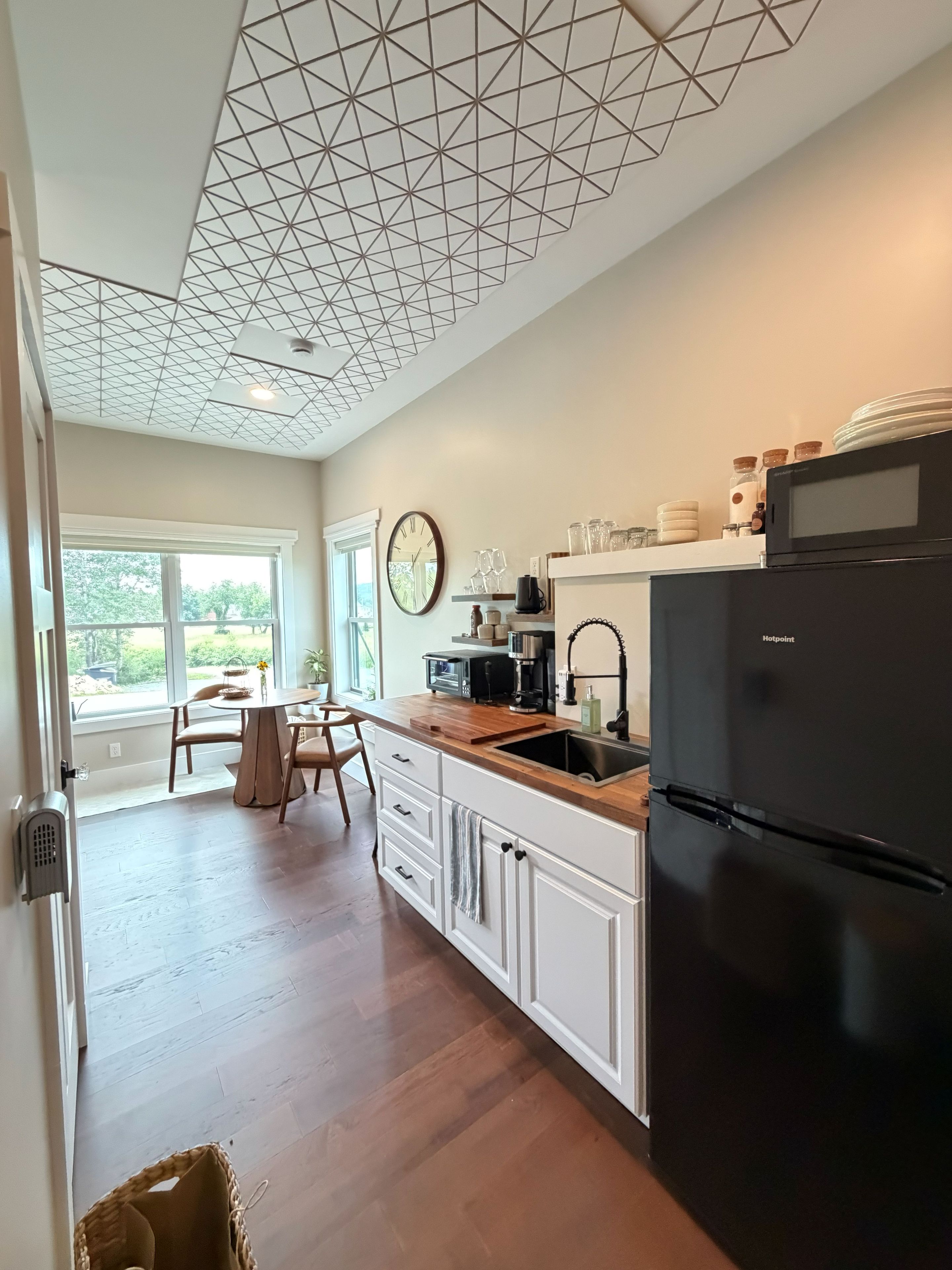 A kitchen with a modern design, featuring a black refrigerator, wooden countertops, and a geometric ceiling pattern.