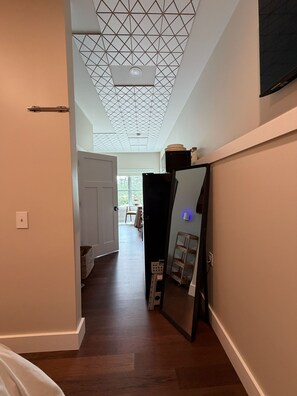 Un couloir avec un plafond au motif géométrique, un réfrigérateur noir et une porte blanche donnant sur une autre pièce.