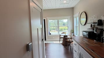 Une cuisine avec un plan de travail en bois, une horloge au mur et une vue sur l’extérieur par la fenêtre.