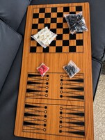 A wooden board game table with checkered and patterned designs, accompanied by bags of game pieces.