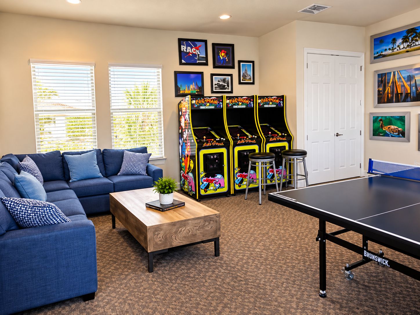 A living room with a blue sofa, a coffee table, a ping pong table, arcade games, and framed pictures on the wall.