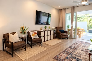 A modern living room with leather armchairs, a flat-screen TV, and a dining area with a view to the outdoors.