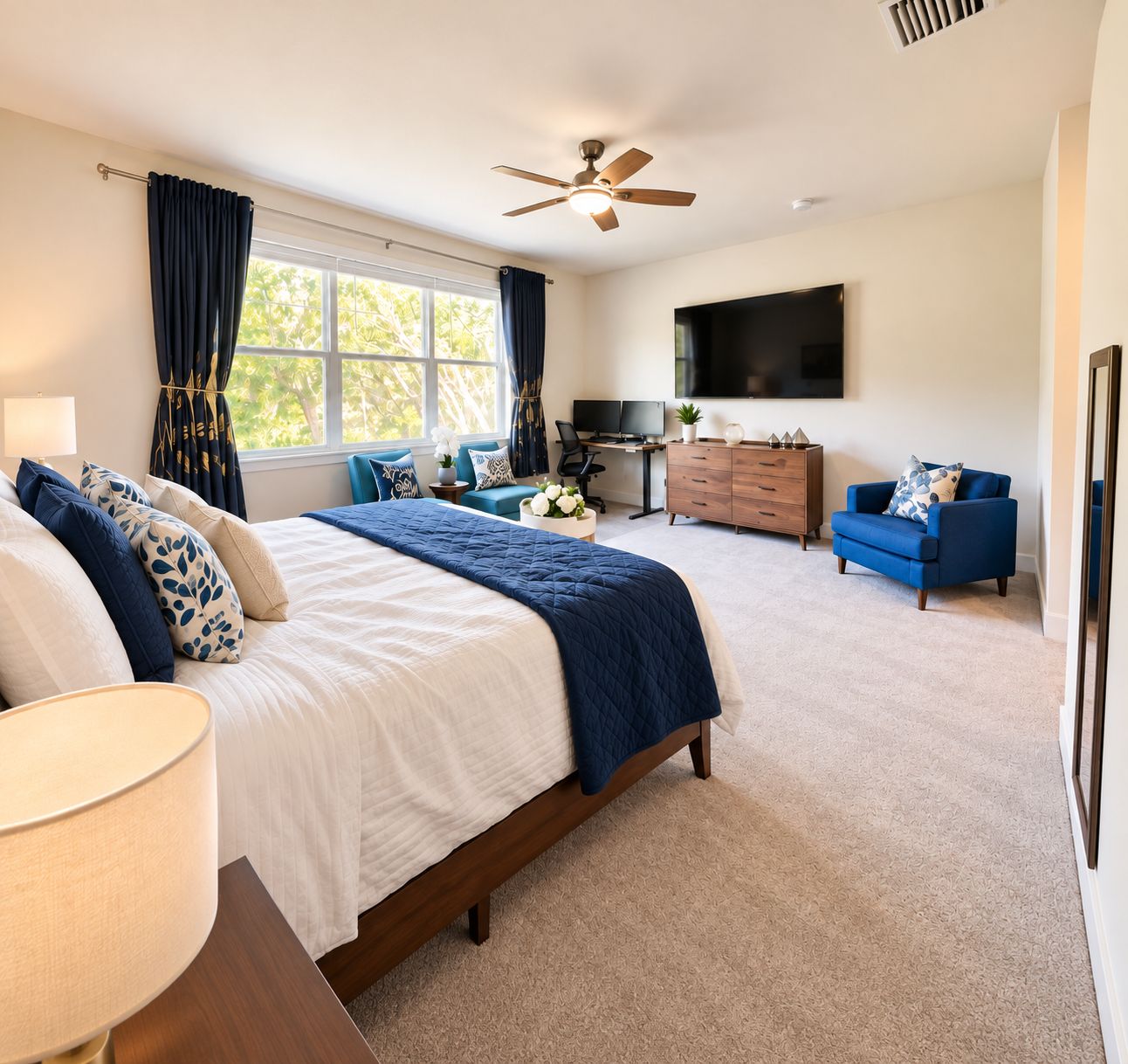 A bedroom with a bed, a desk, a chair, a TV, and a ceiling fan.