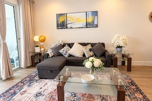 Uma sala de estar moderna com sofá seccional, mesa de centro de vidro e almofadas decorativas.