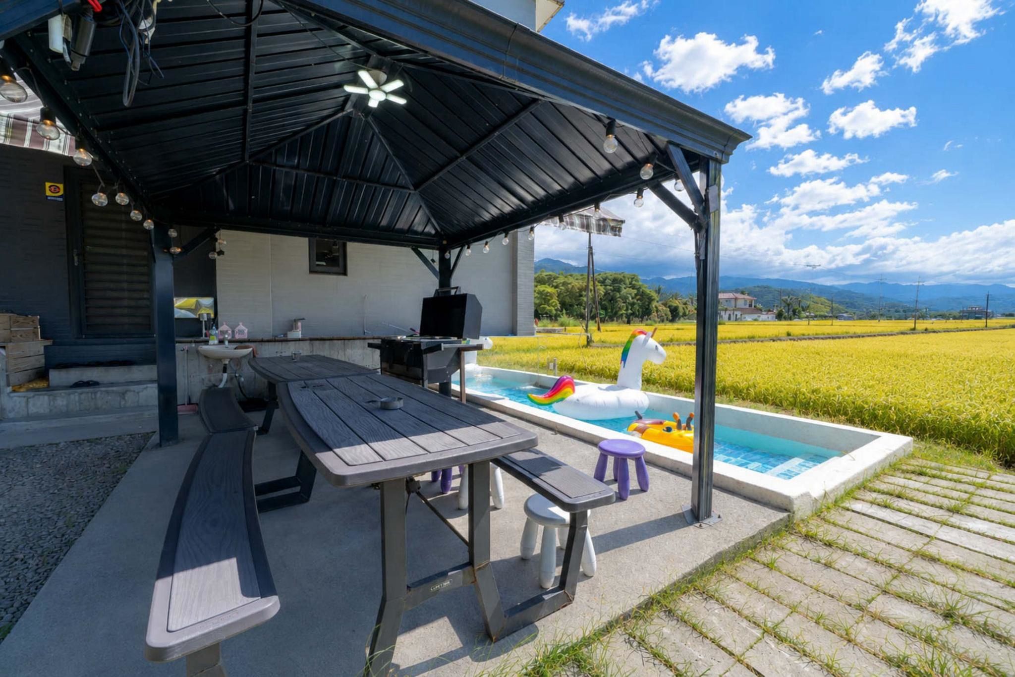 An outdoor patio with a pool, a covered seating area, and a view of a green field.