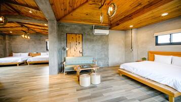 A modern hotel room with a wooden ceiling, a large bed, two smaller beds, a sofa, a table with board games, and a window.