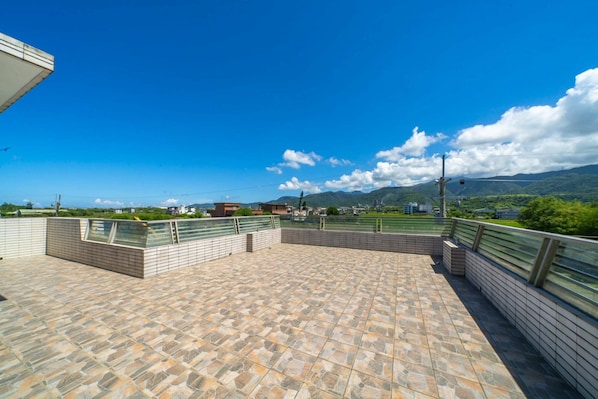 A rooftop terrace with a stone tile floor, metal railings, and a view of distant buildings and mountains. - H Villa YiLan (Dongshan)