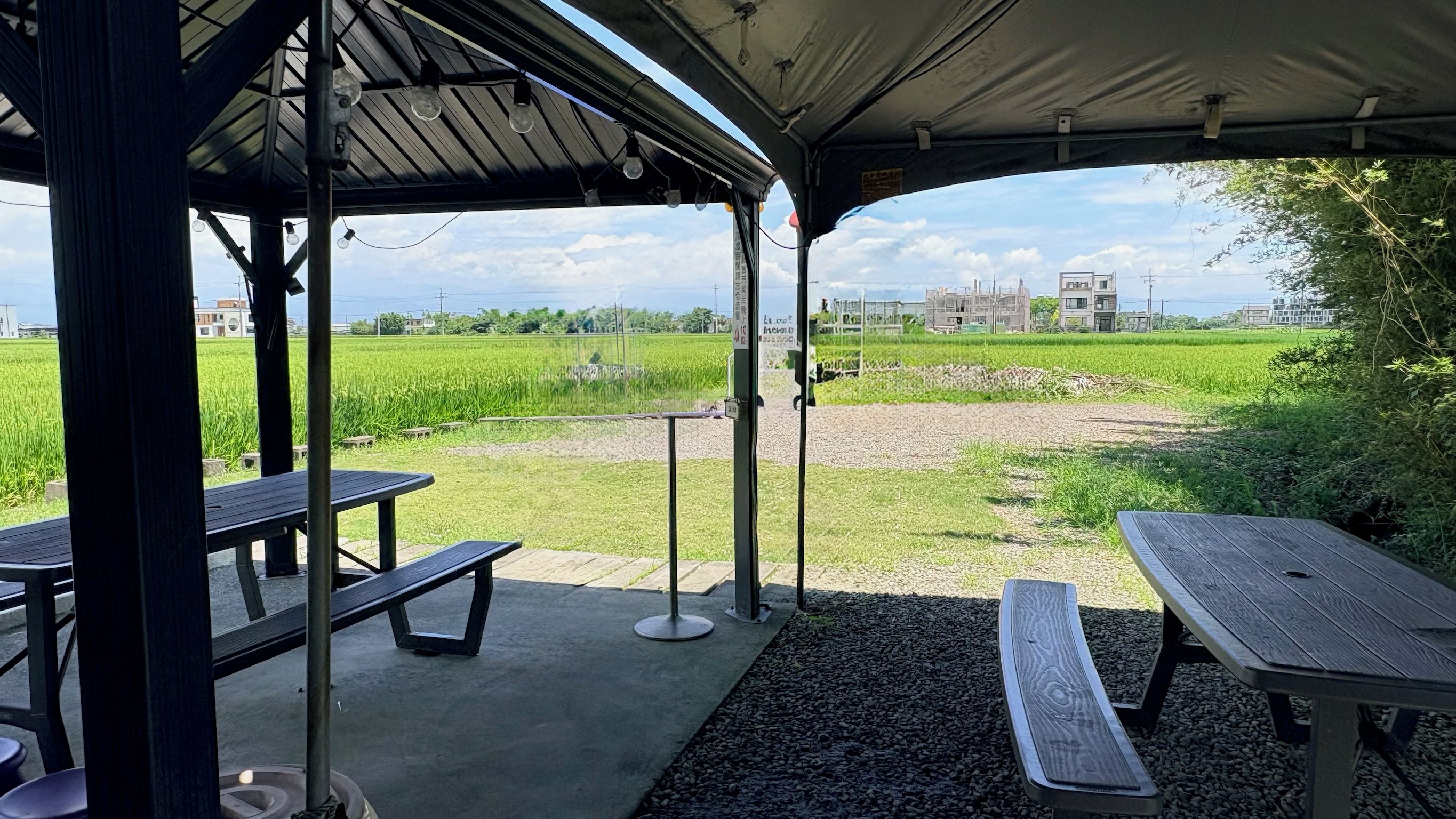 An outdoor pavilion with picnic tables and a view of a green field.