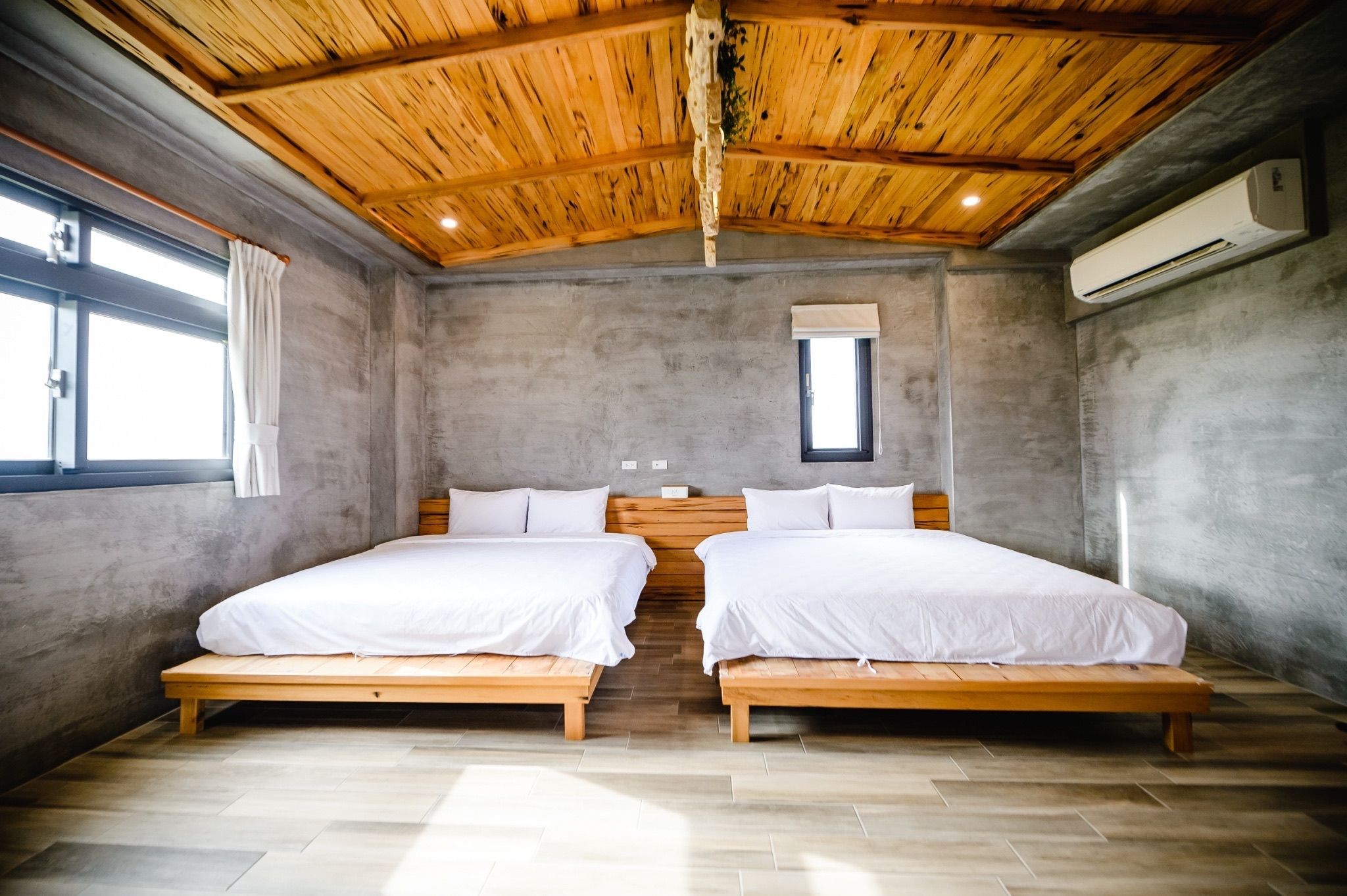 A room with two beds, a wooden ceiling, and a window.