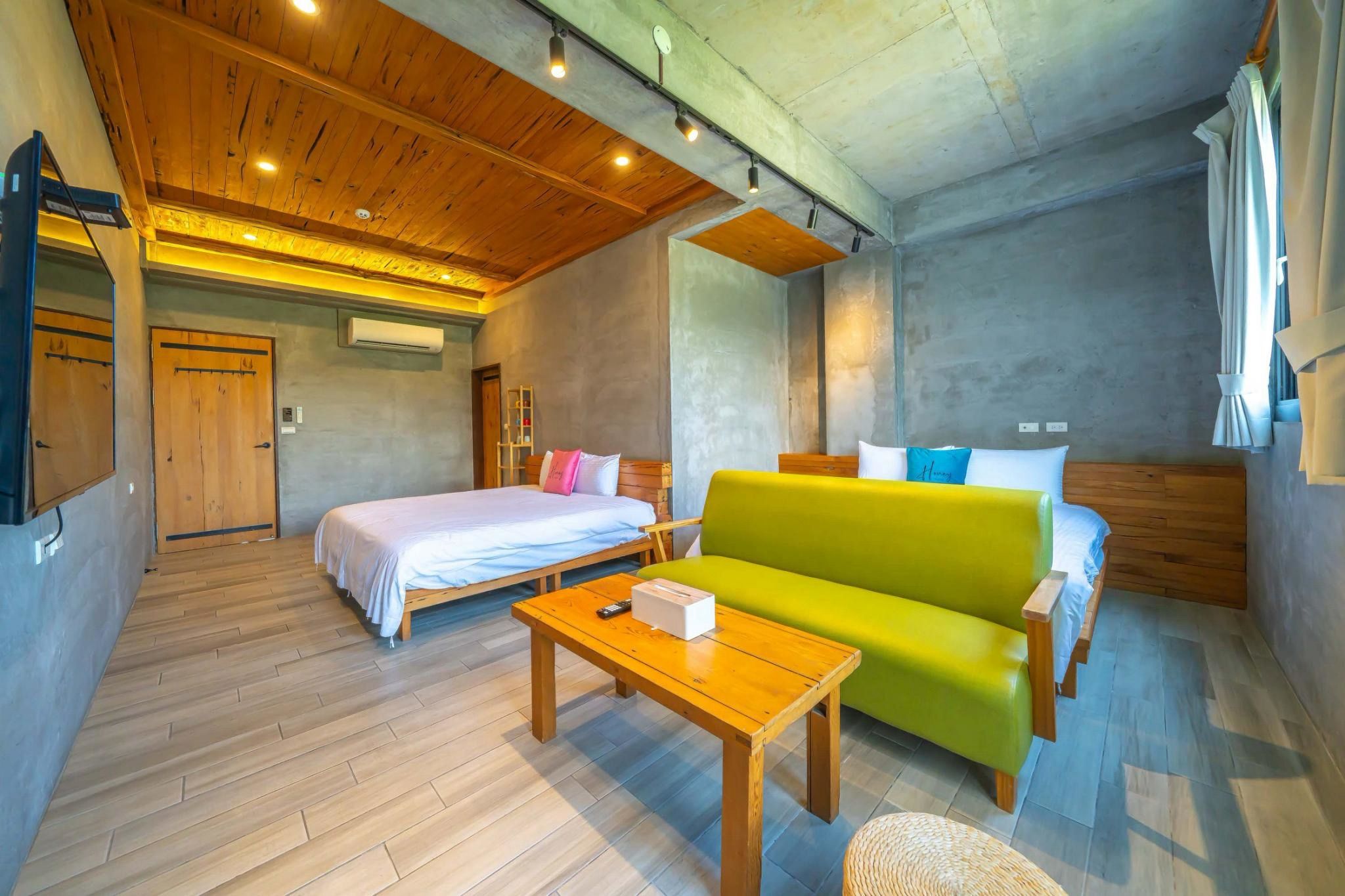 Habitación de hotel con techo de madera, dos camas, un sofá verde, una mesa de madera y una ventana con cortinas.