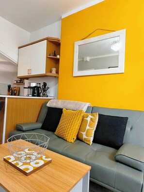 A compact living space with a kitchenette, a sofa with cushions, and a dining table with a decorative item. - Clean, Cosy, Homely - city access right outside (Edinburgh)