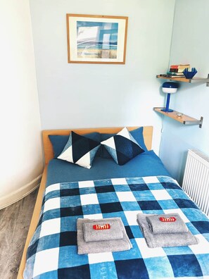 A neatly made bed with a checkered blue and white bedspread, two pillows, and two folded towels on the bed. - Clean, Cosy, Homely - city access right outside (Edinburgh)