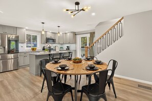 Een moderne keuken met een centraal eiland, roestvrijstalen apparatuur en een eethoek met zwarte stoelen en een houten tafel.