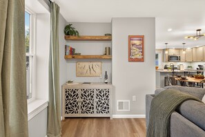 A modern living room with a grey sofa, a wooden cabinet with decorative cutouts, a bookshelf with books, and a wall-mounted picture. - Newly Remodeled | Near Wineries | Sleeps 10 (Dundee)
