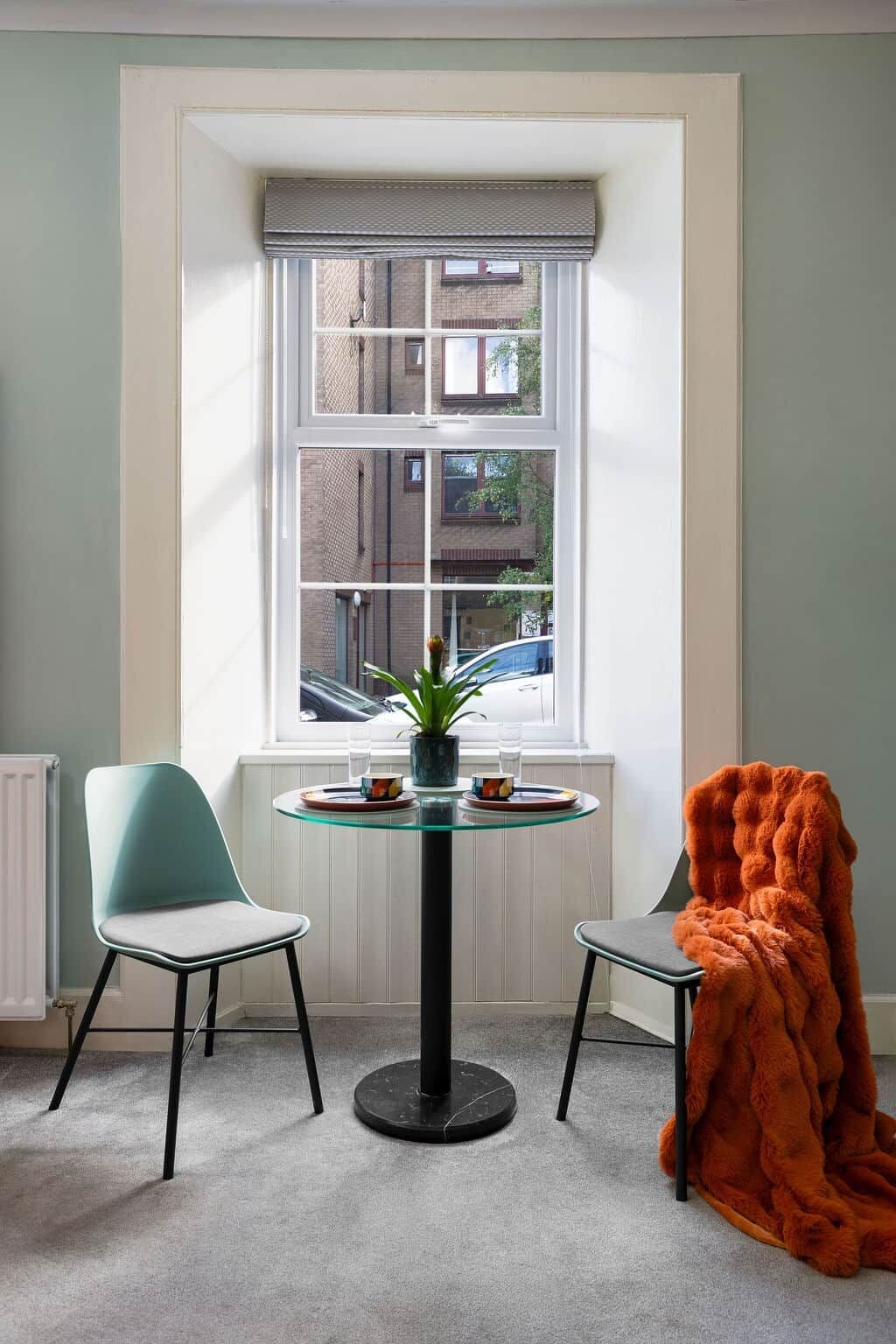A room with a window, two chairs, a table with a plant, and a blanket.
