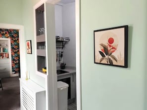 Eine Küche mit weißen Schränken, einem Spülbecken und einer Arbeitsplatte. An der Wand hängt ein gerahmtes Bild.