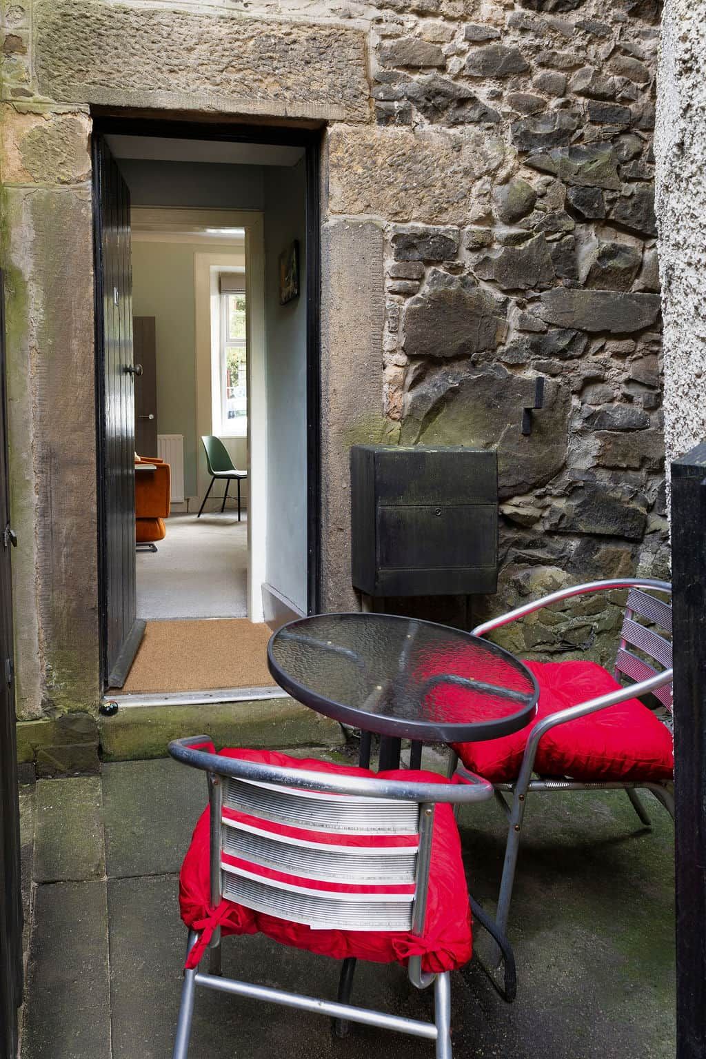 An outdoor seating area with a table and chairs, a stone wall, and a door leading to an interior space.