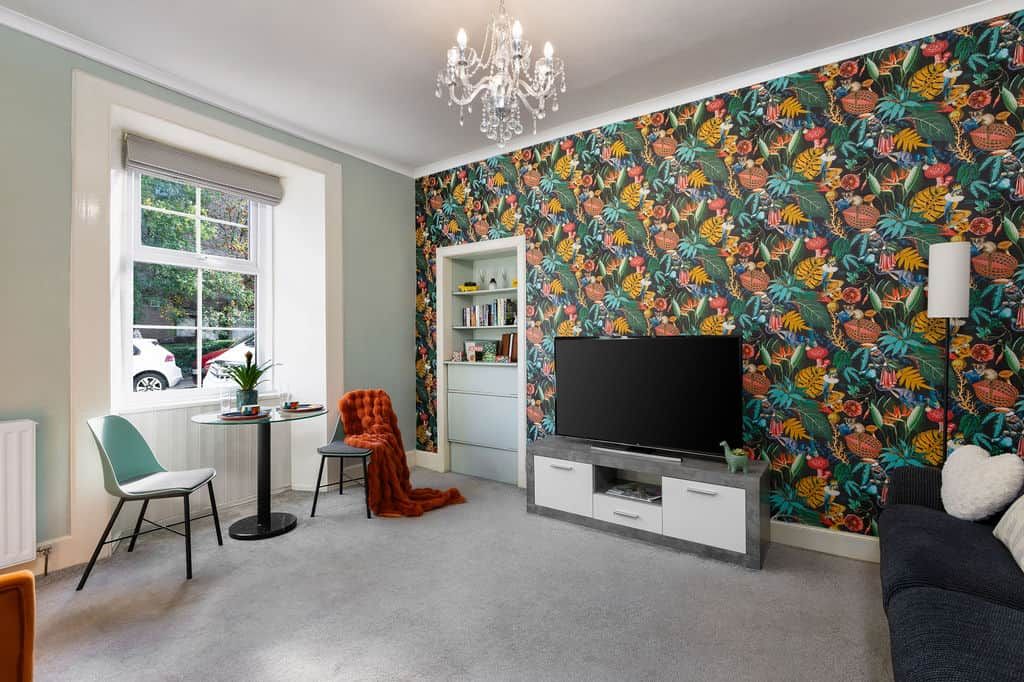 Ein Wohnzimmer mit Fernseher, Bücherregal, einem Fenster mit Aussicht und einer Wand mit Muster.