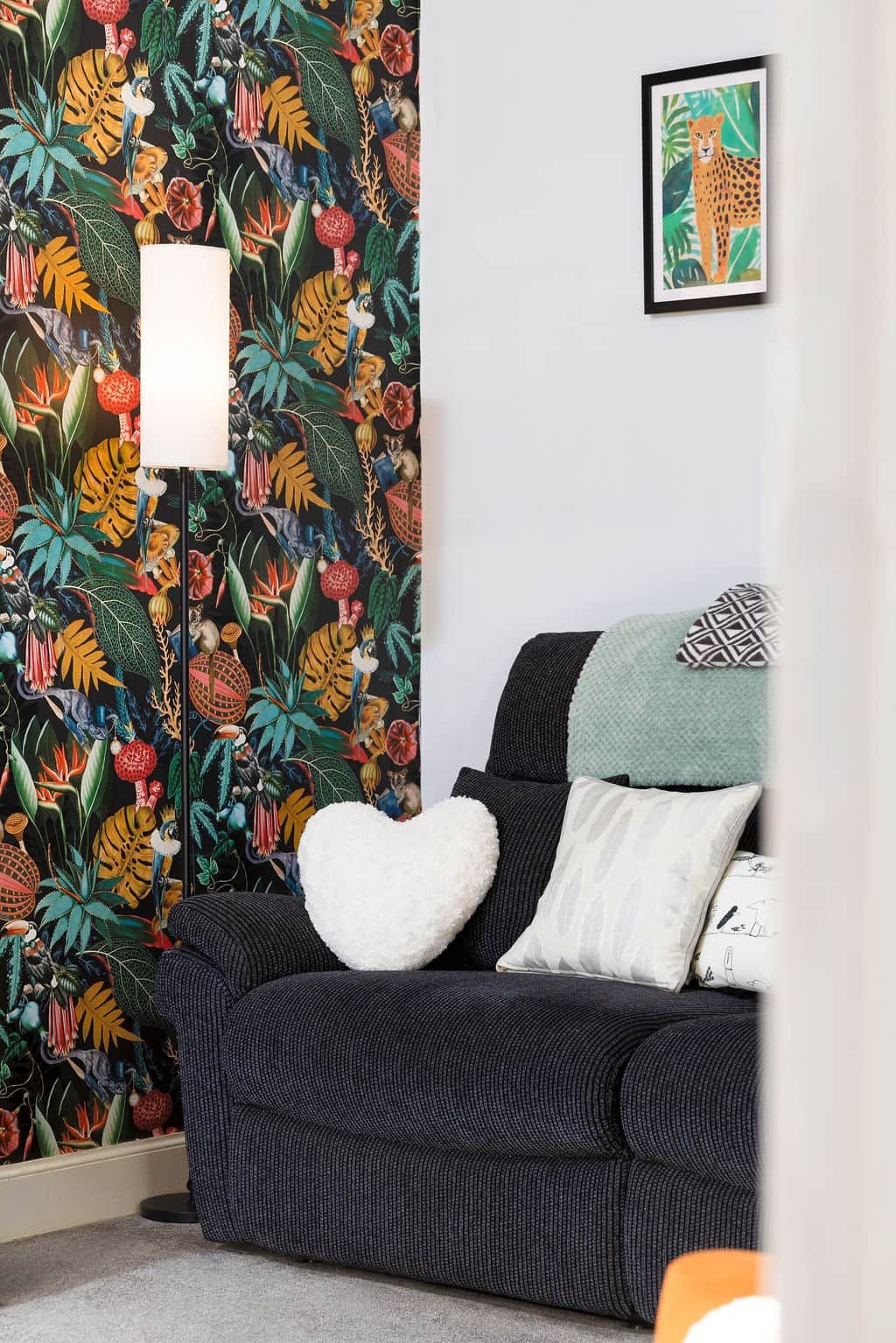 Una habitación con papel tapiz estampado, un cuadro en la pared y un sofá oscuro con cojines.