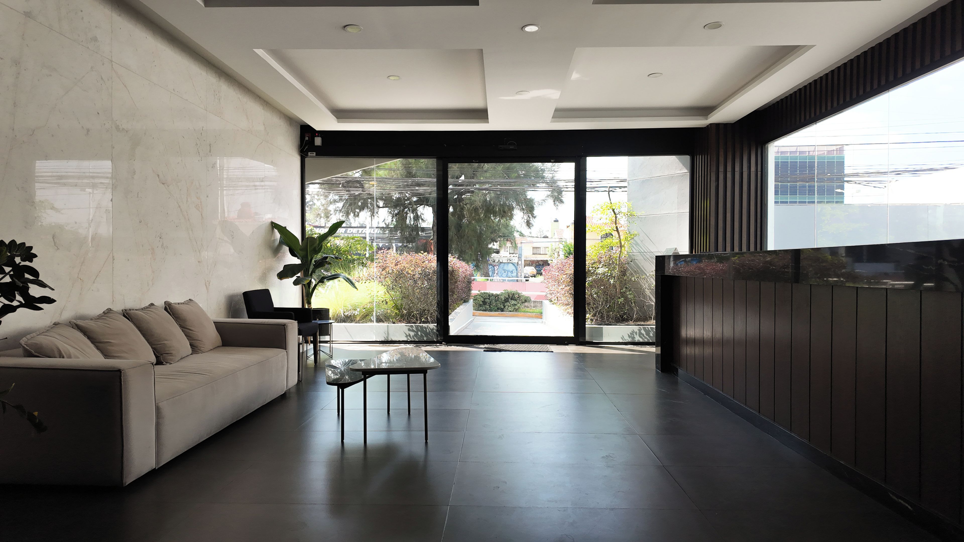 A modern living room with a sofa, a coffee table, and a large window offering a view of the outdoors.
