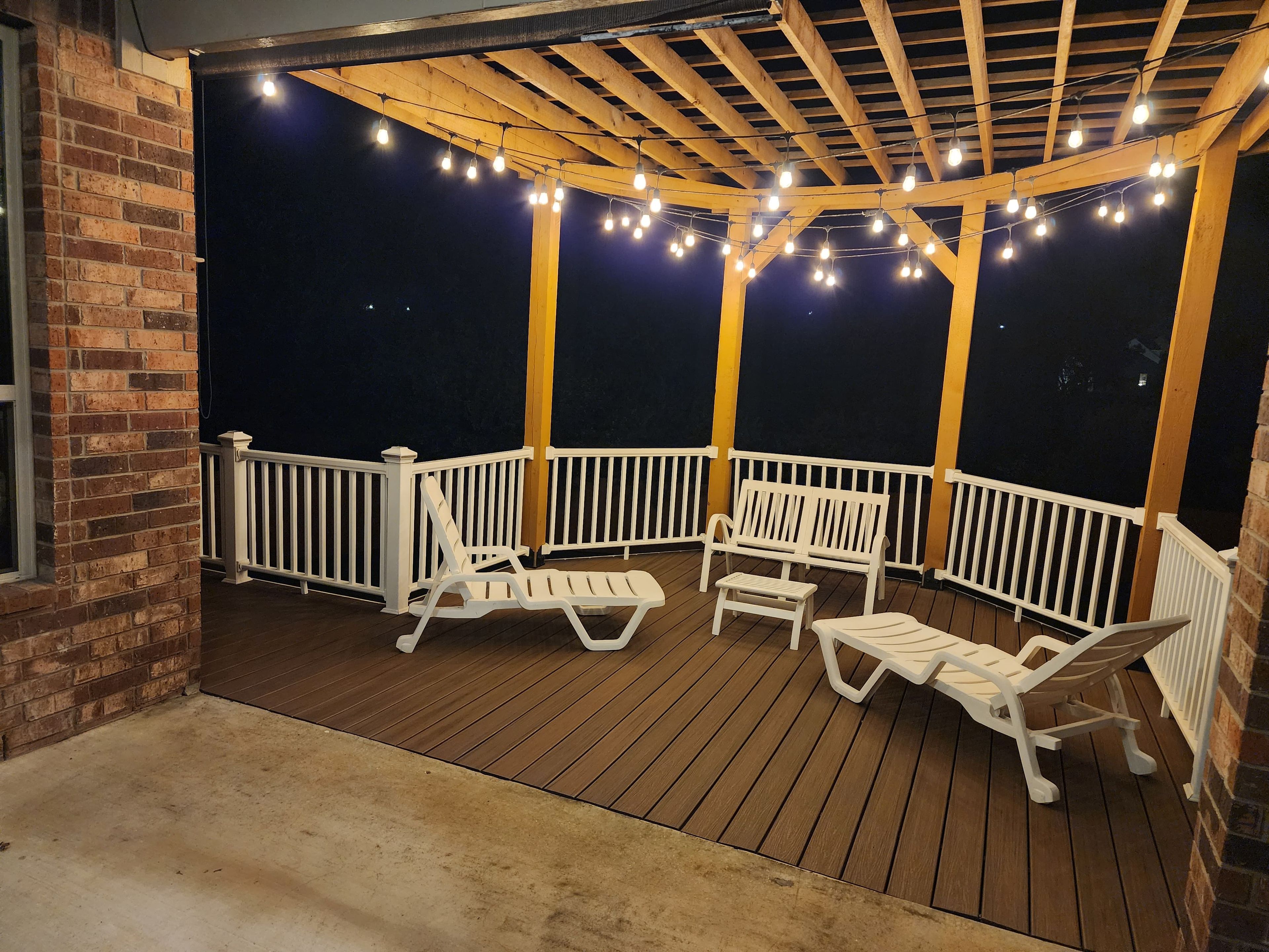 Une terrasse extérieure avec un plancher en bois, des rampes blanches et des guirlandes lumineuses.