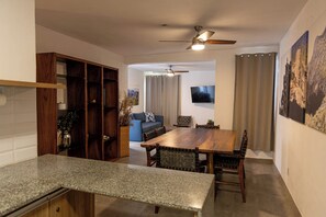 A dining area with a wooden table and chairs, a ceiling fan, and a television mounted on the wall. - San Luisito departamentos (Puerto Vallarta)